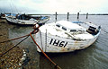 Old white clinker-built fishing boat moored by the Suffolk shore under a leaden sky
