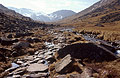 On the rocky path to Sty Head in the English Lake District, in strong spring sunshine, with Scafell Pike and Lingmell in the distance under light snow